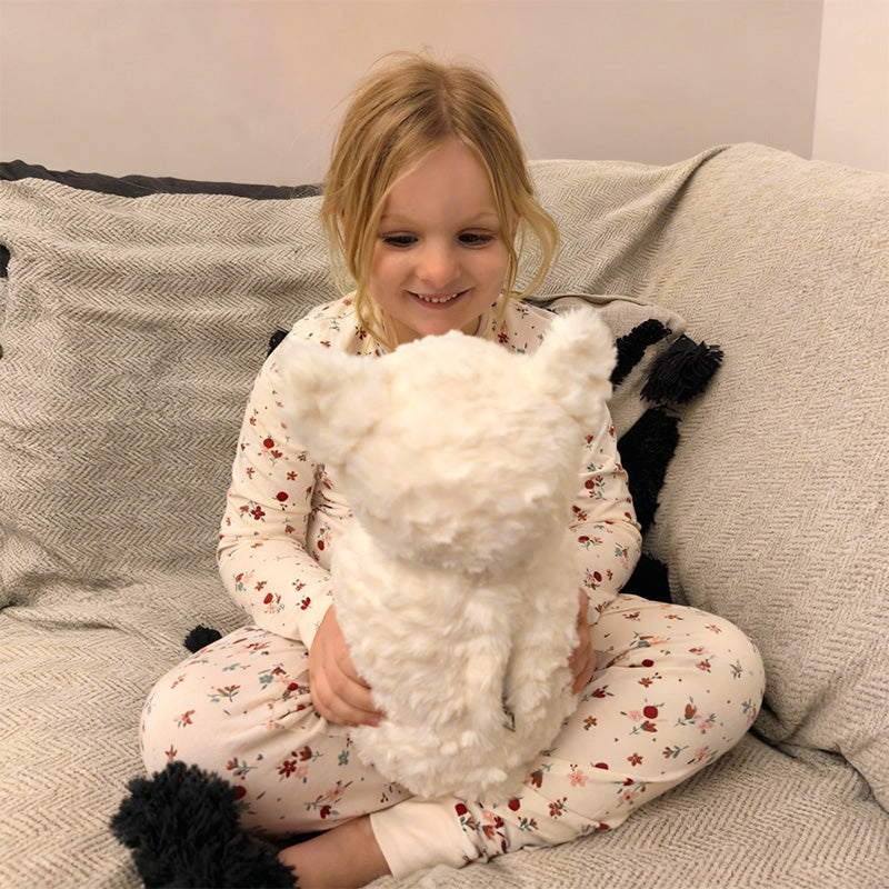 Child holding a fluffy white AI cat toy on a couch