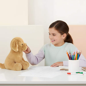 Young girl playing with TalkiPal's AI plush dog toy at a table with colored pencils and a notebook.