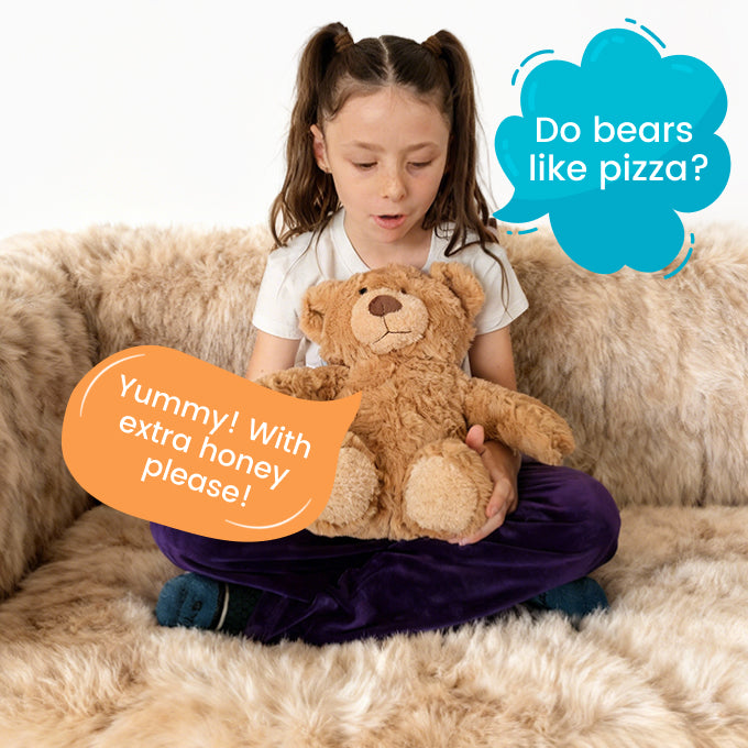 Child holding TalkiPal AI bear toy with text bubbles on a beige couch