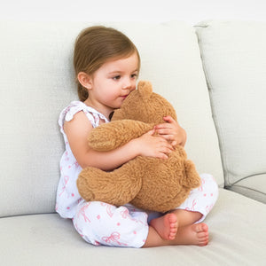 Child hugging TalkiPal AI toy Benny the bear on a light-colored couch