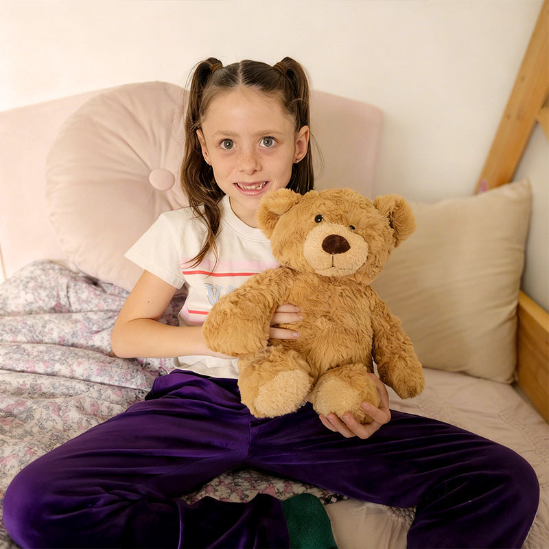 Young girl holding TalkiPal's AI plush bear toy on a bed with pillows and a wooden headboard